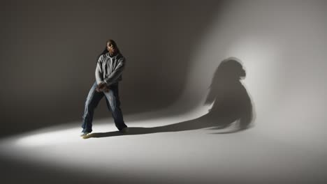 Full-Length-Studio-Portrait-Shot-Of-Young-Woman-Dancing-Casting-Shadow-With-Low-Key-Lighting-Against-Grey-Background-3